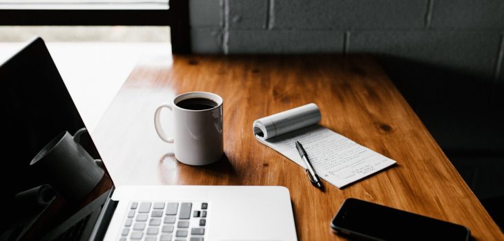 MacBook Pro, white ceramic mug,and black smartphone on table