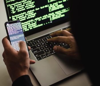 Free Unrecognizable hacker with smartphone typing on laptop at desk Stock Photo