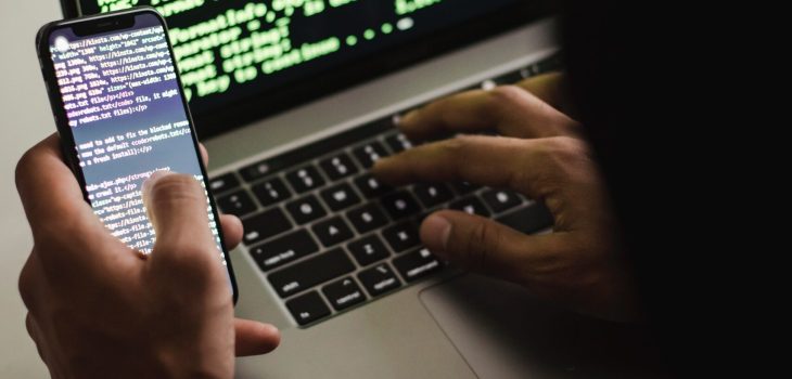 Free Unrecognizable hacker with smartphone typing on laptop at desk Stock Photo