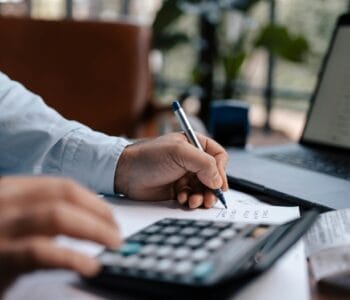 Free A person calculating finances with a calculator and pen on a desk indoors. Stock Photo