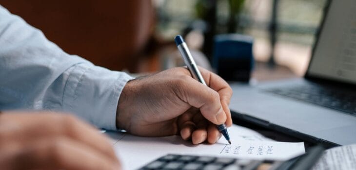 Free A person calculating finances with a calculator and pen on a desk indoors. Stock Photo