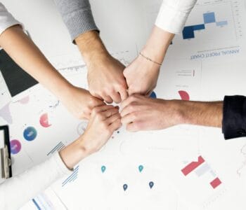Free Colleagues celebrate success with a fist bump over financial charts depicting teamwork and unity. Stock Photo