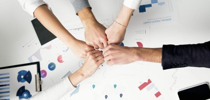 Free Colleagues celebrate success with a fist bump over financial charts depicting teamwork and unity. Stock Photo