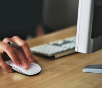 Free A hand using a wireless mouse at a modern desk setup with a computer and keyboard. Stock Photo