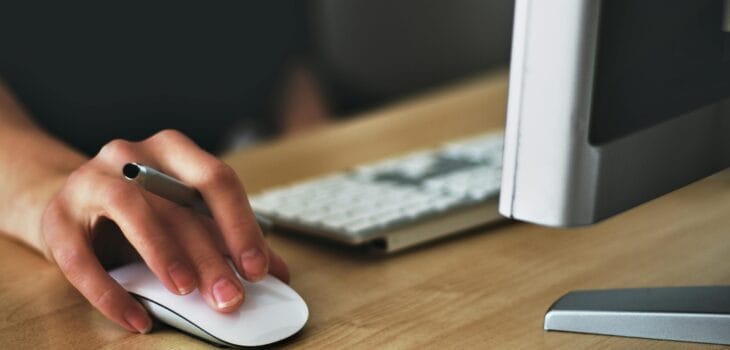 Free A hand using a wireless mouse at a modern desk setup with a computer and keyboard. Stock Photo