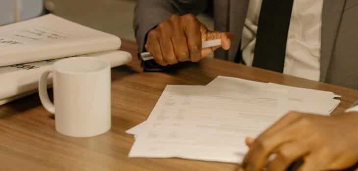Free Close-up of a businessman holding and reviewing documents on a wooden desk. Stock Photo