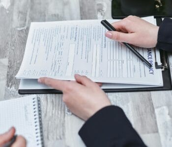 Free Close-up of hands analyzing insurance policy paperwork with pen on table. Stock Photo